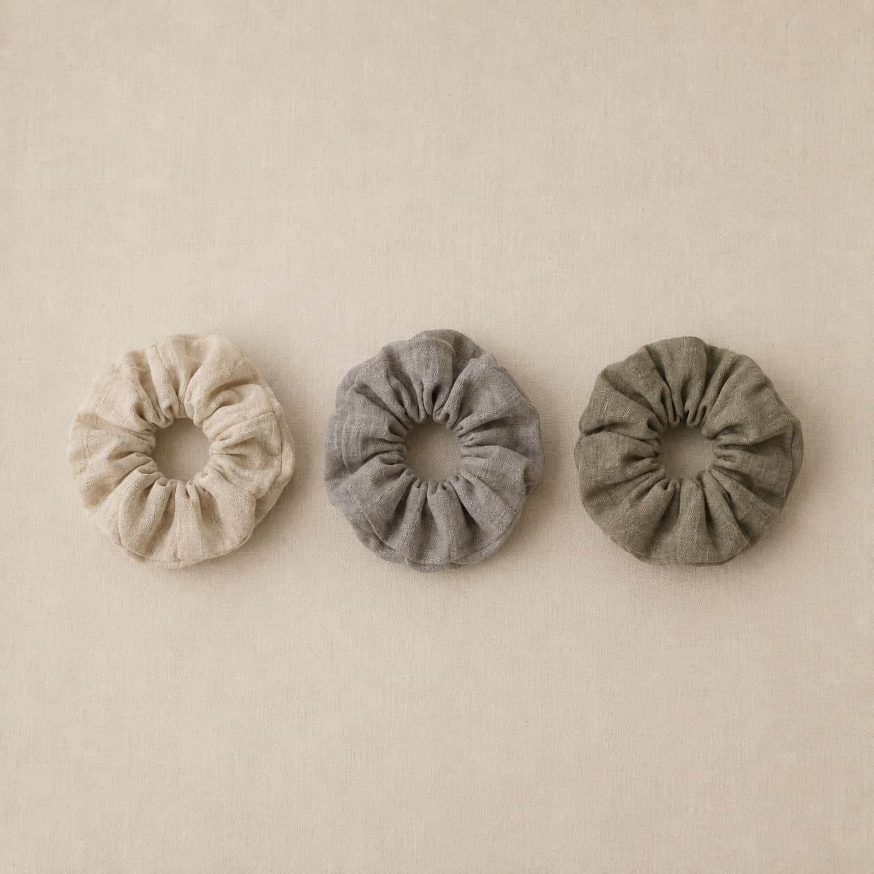 Three gathered fabric hair ties in different neutral tones laid in a row.