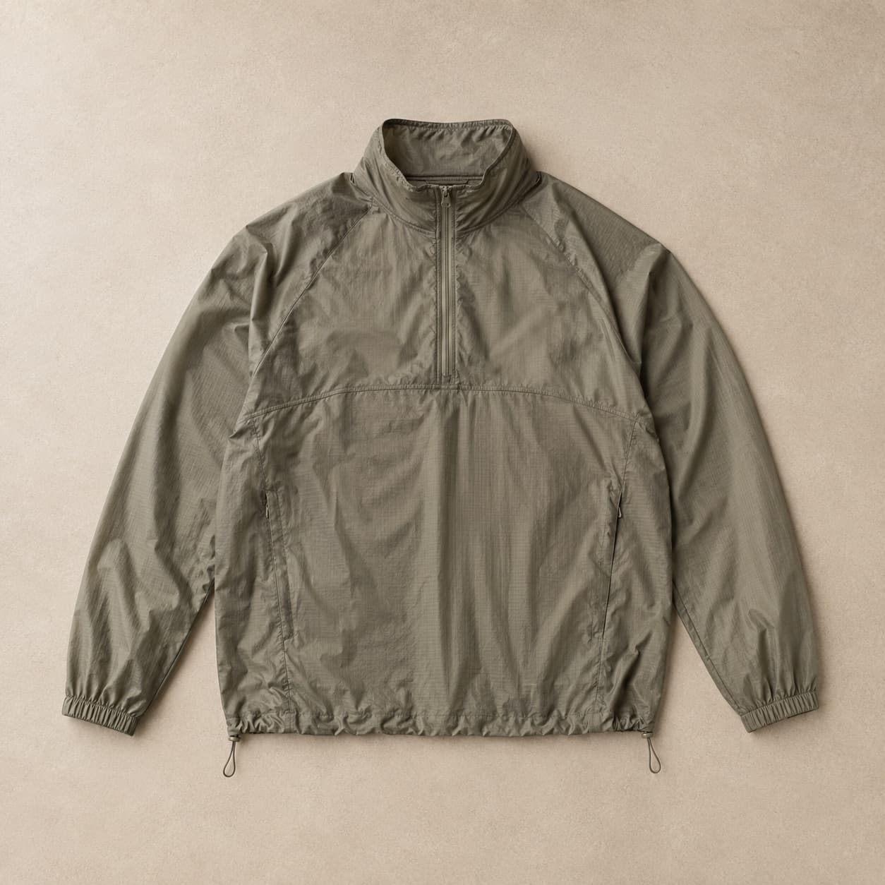 Olive-grey half-zip windbreaker laid flat with the hem drawcord visible.