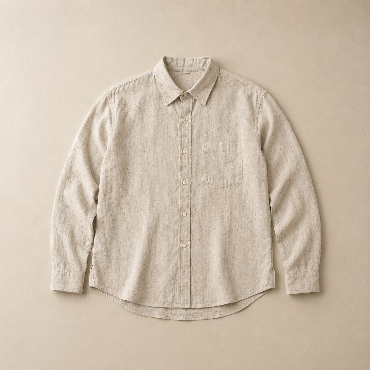 Unbleached natural linen shirt laid flat with visible dark flecks in the weave.